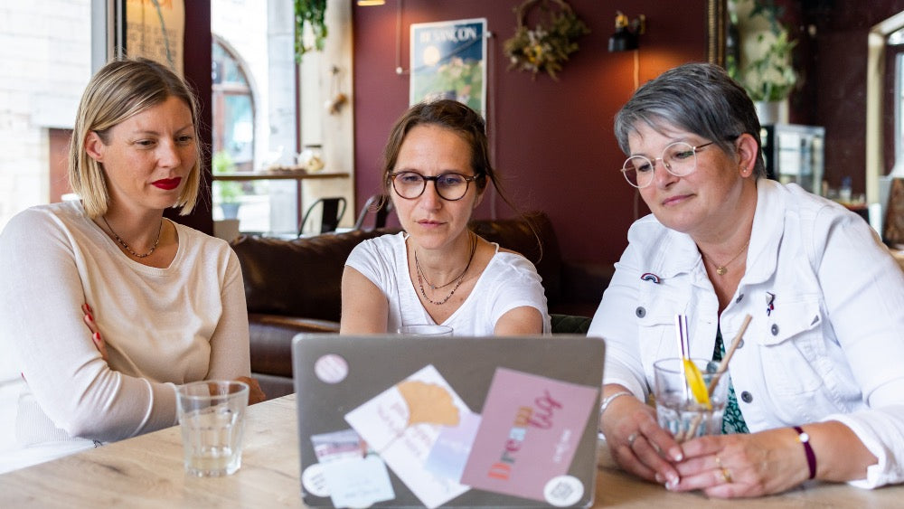 Fanny, Maud et Laurence travaillant ensemble sur un ordinateur, créant le nouveau site Les Mots Doux avec passion et dévouement.